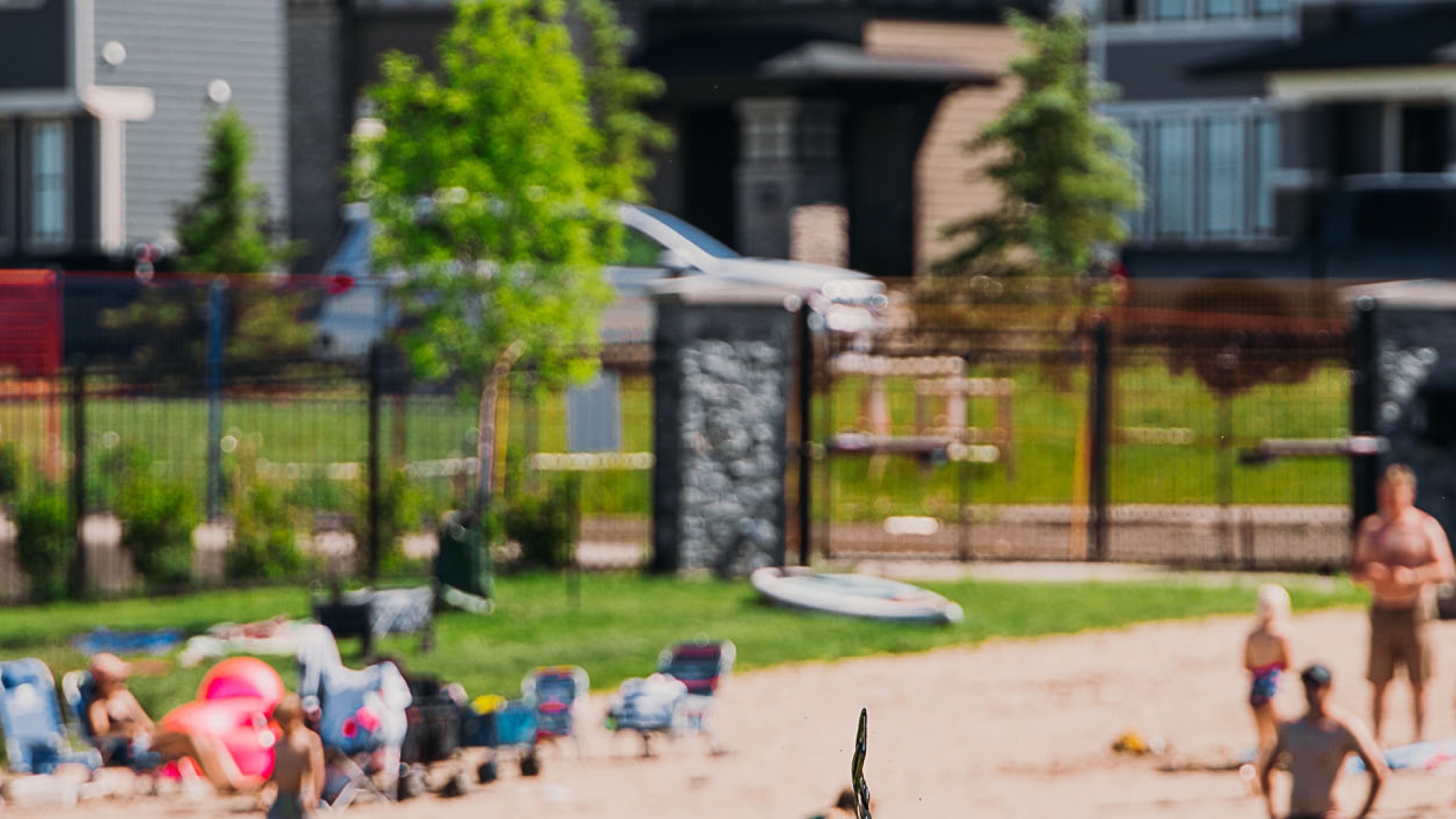 Beachgoers relax on a sandy shore near modern houses.